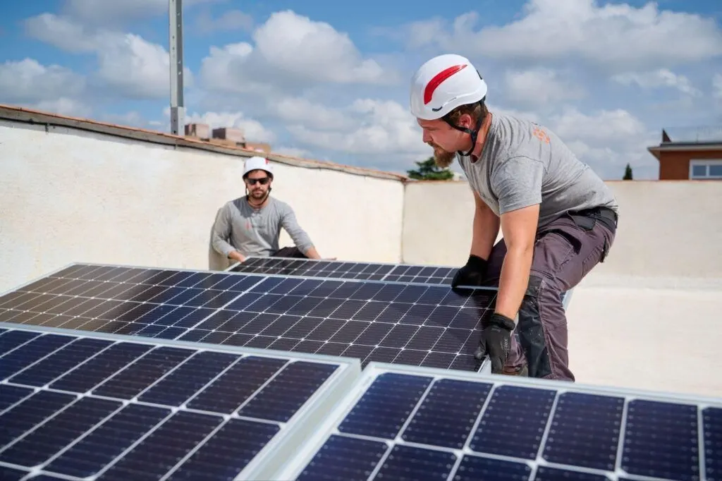 Dos operarios con casco colocan paneles solares en la azotea de una vivienda